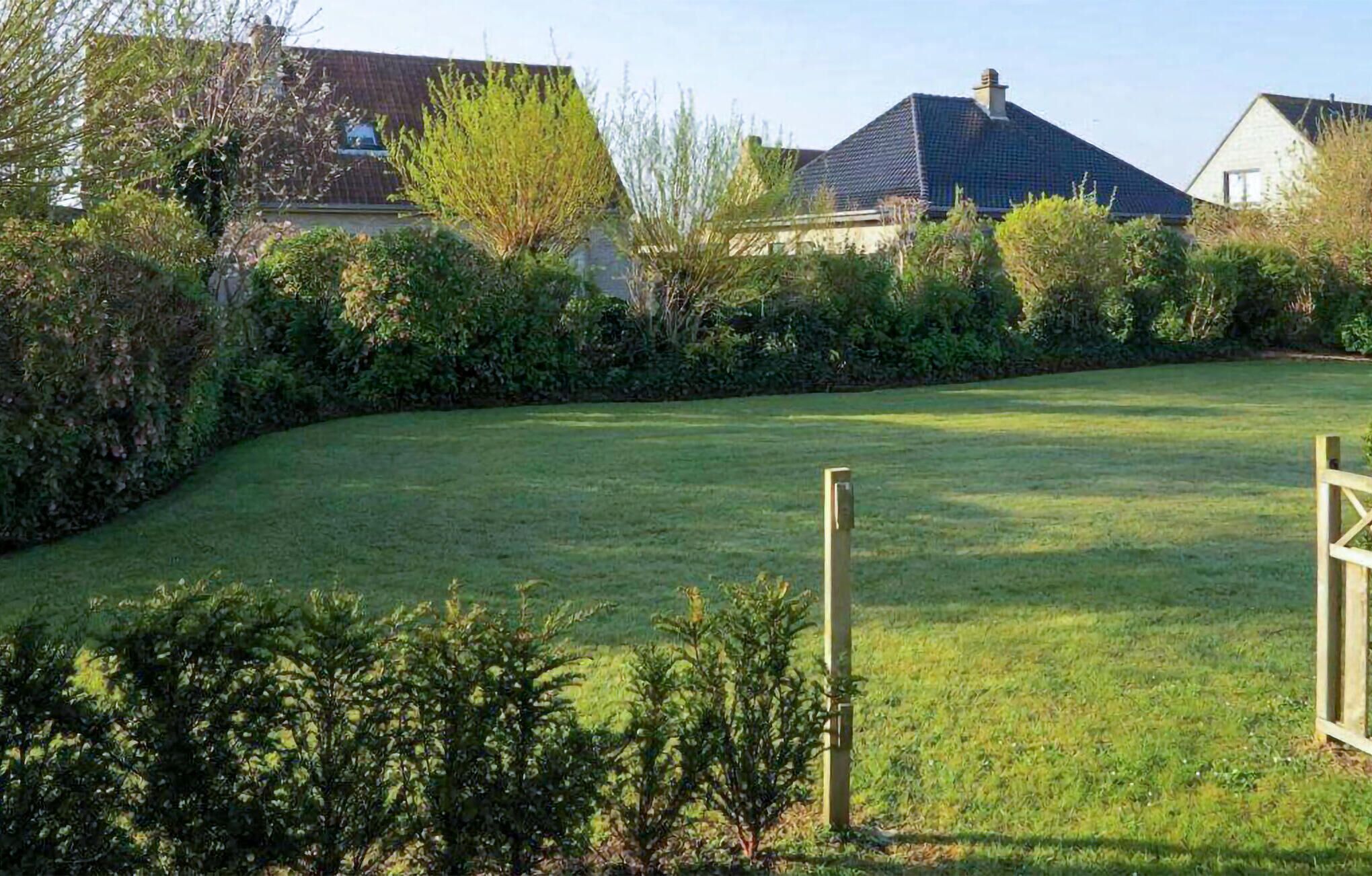 A well-maintained grassy area with a wooden fence, surrounded by dense shrubbery and trees.