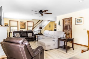 A living room with a brown leather sofa, a light-colored sectional sofa, a wooden coffee table, and a ceiling fan.