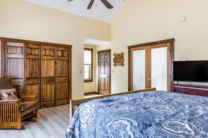 A bedroom with a large bed, wooden wardrobe, a television, and a small table with a pillow.