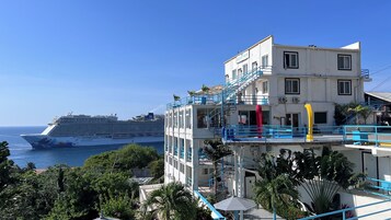 Un edificio de varios pisos con balcones y una vista de un crucero al fondo.