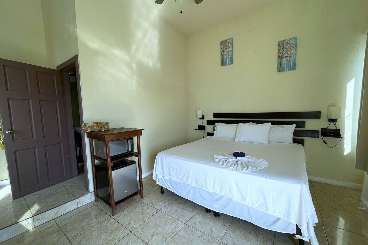 Une chambre d’hôtel comprenant un lit, une table de chevet en bois avec un micro-ondes, une porte et deux lampes fixées au mur.