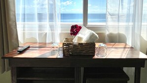 Zona pranzo con tavolo, sedie, telecomando, bicchiere e cesto con fiori e tovagliolo.