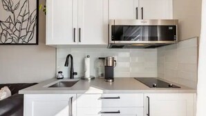 A modern kitchen with white cabinets, a stainless steel microwave, a coffee maker, and a sink.