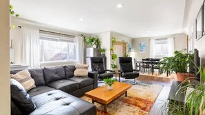 A modern living room with a black leather sofa, a wooden coffee table, and a large window.