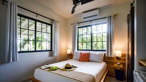 Habitación de hotel con una cama grande, dos mesitas de noche con lámparas, un ventilador de techo y ventanas amplias con cortinas.