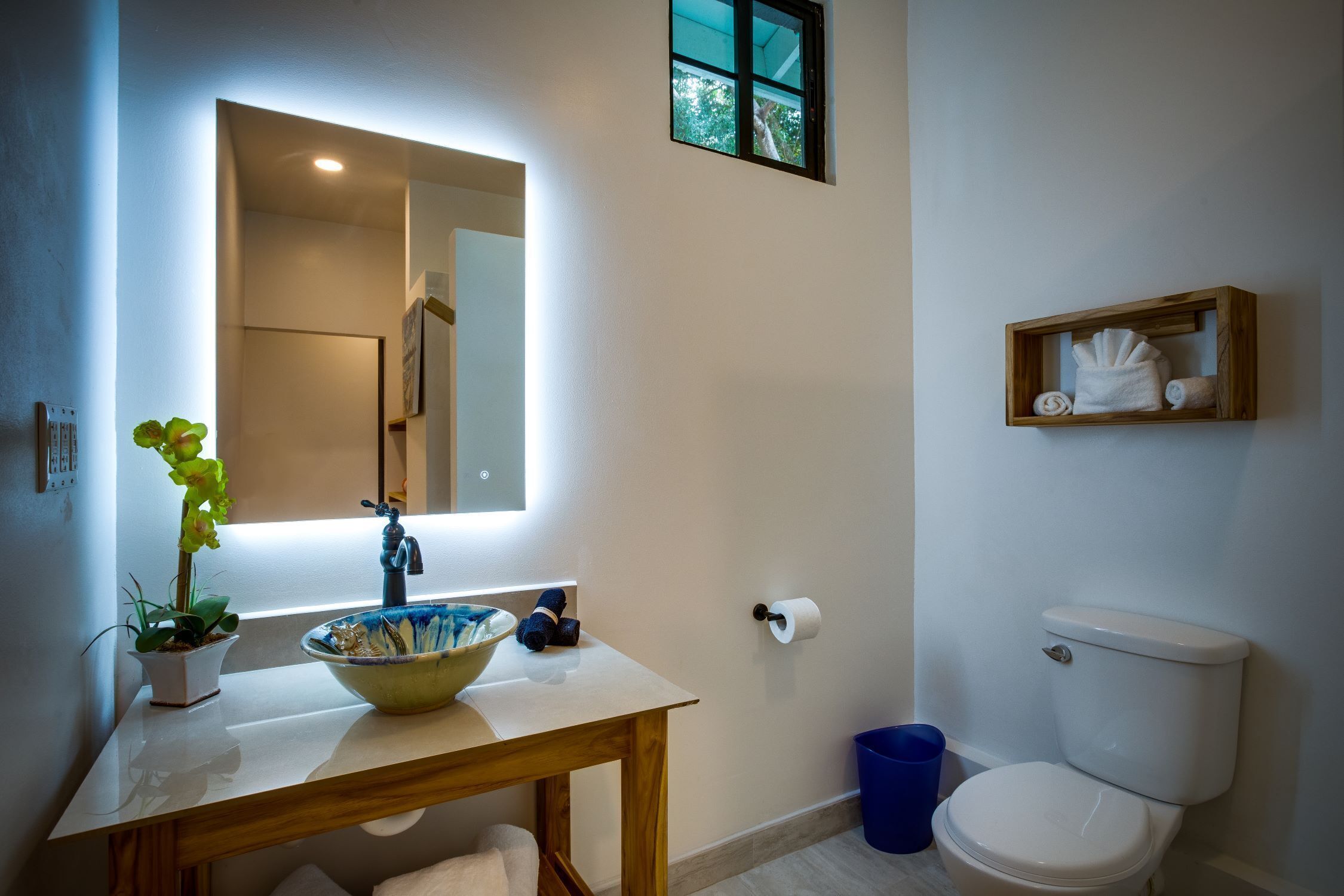 A bathroom with a sink, mirror, toilet, and a small shelf with towels.