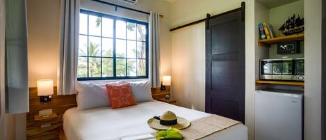 Un dormitorio ordenado con cama, lámparas de noche, un refrigerador pequeño y una ventana con cortinas.