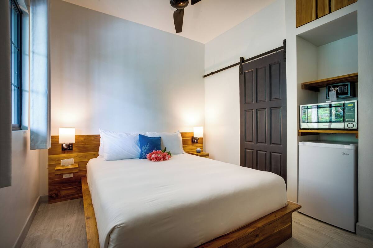 Ein Hotelzimmer mit einem Bett, Nachttischlampen, einem Holznachttisch, einem kleinen Kühlschrank und einem Schiebetürenschrank.