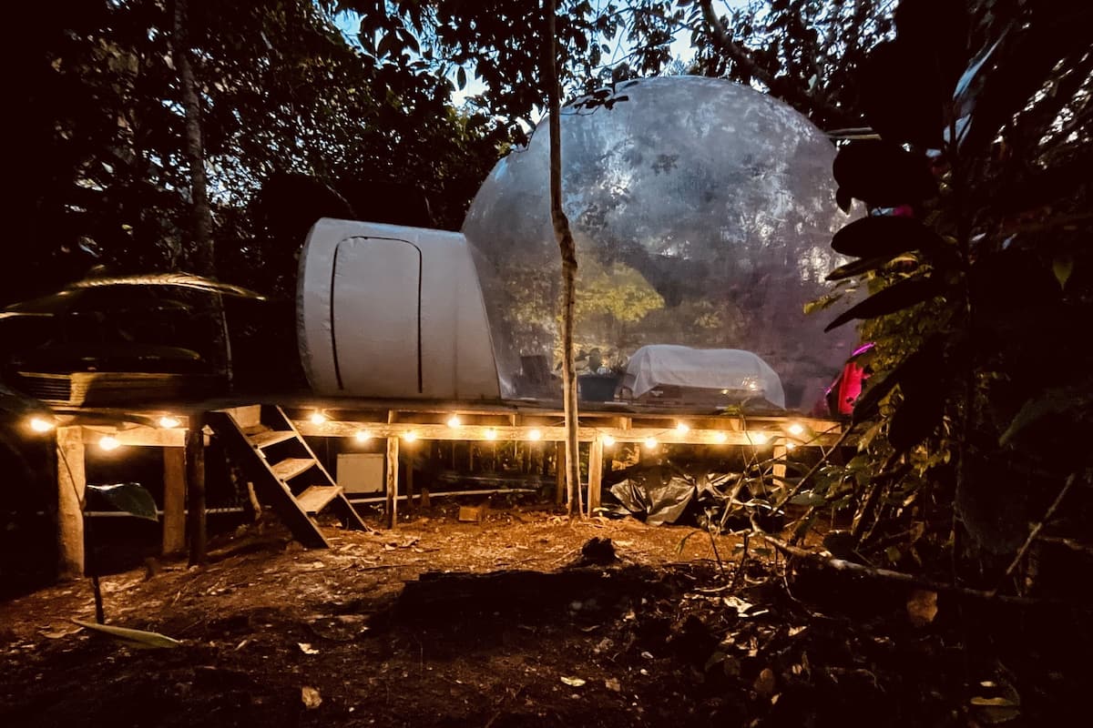 A large spherical structure in a forested area with a table and chairs under string lights.