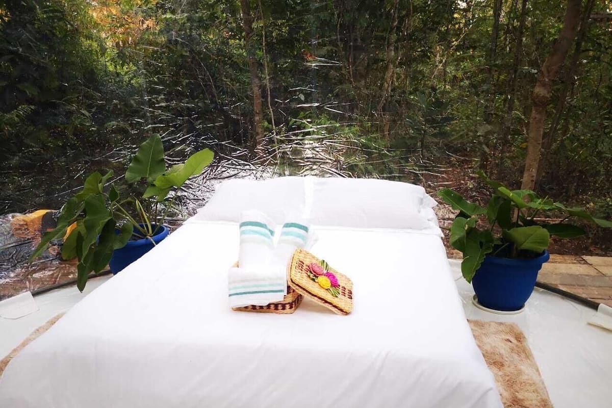 A bed with a white sheet, two towels, and a basket with fruit.