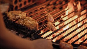 Ein Detailaufnahme eines Grills, auf dem Fleisch über offenem Feuer gegrillt wird.