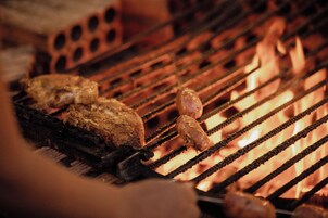 Primer plano de una parrilla con carne asándose sobre fuego abierto.