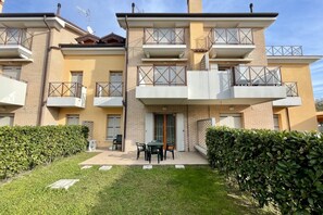 Ein zweistöckiges Mehrfamilienhaus mit Balkonen, einer kleinen Terrasse mit Tisch und Stühlen sowie einer gepflegten Hecke.