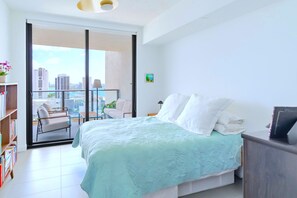 Relax in a serene bedroom with a large bed, sliding glass door to a city view balcony, and a cozy reading nook.