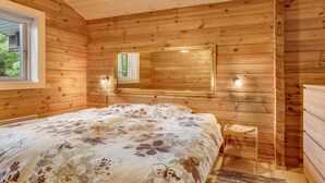 Dormitorio de cabaña de madera con cama, espejo y una mesita.