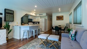 A modern kitchen with white cabinets, a central island, and a dining area with a table and chairs. - Summertime Bayou Houseboat Oasis: Fish, Hot tub, Kayak (Morgan City)