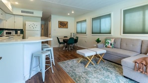 A modern kitchen with white cabinets, a central island with stools, a dining area with a table and chairs, and a living area with a sofa and a rug. - Summertime Bayou Houseboat Oasis: Fish, Hot tub, Kayak (Morgan City)