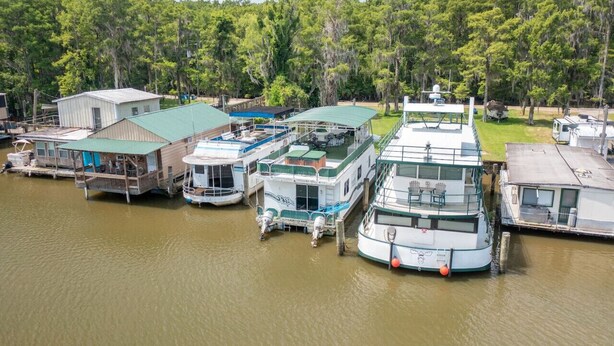 A marina with several houseboats docked, surrounded by lush greenery. - Summertime Bayou Houseboat Oasis: Fish, Hot tub, Kayak (Morgan City)