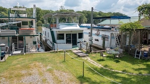 A marina with several boats docked, a covered area with seating, and a small outdoor seating area with tables and chairs. - Summertime Bayou Houseboat Oasis: Fish, Hot tub, Kayak (Morgan City)