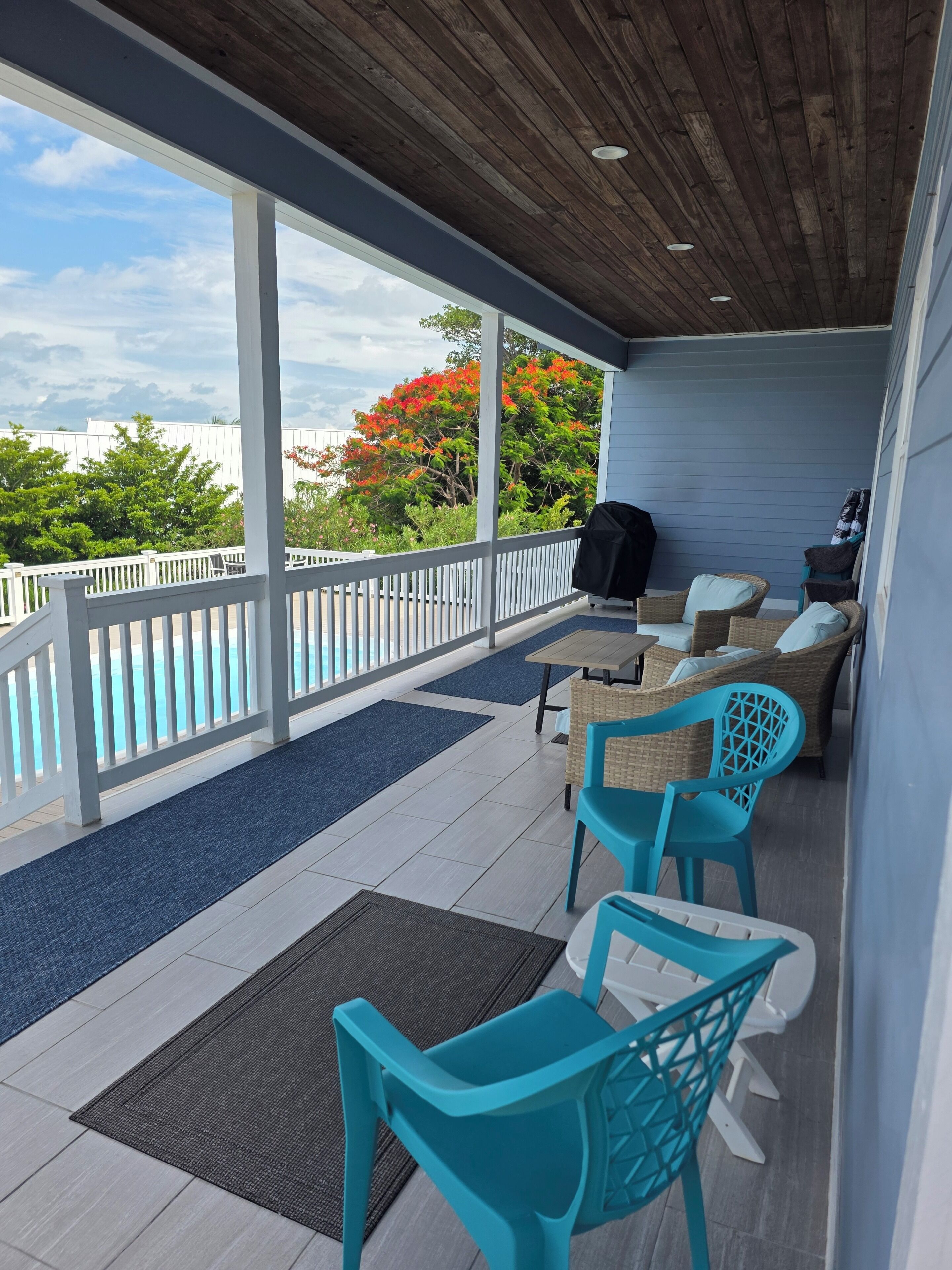 A covered outdoor area with a pool, seating, and a view of the sky and trees.