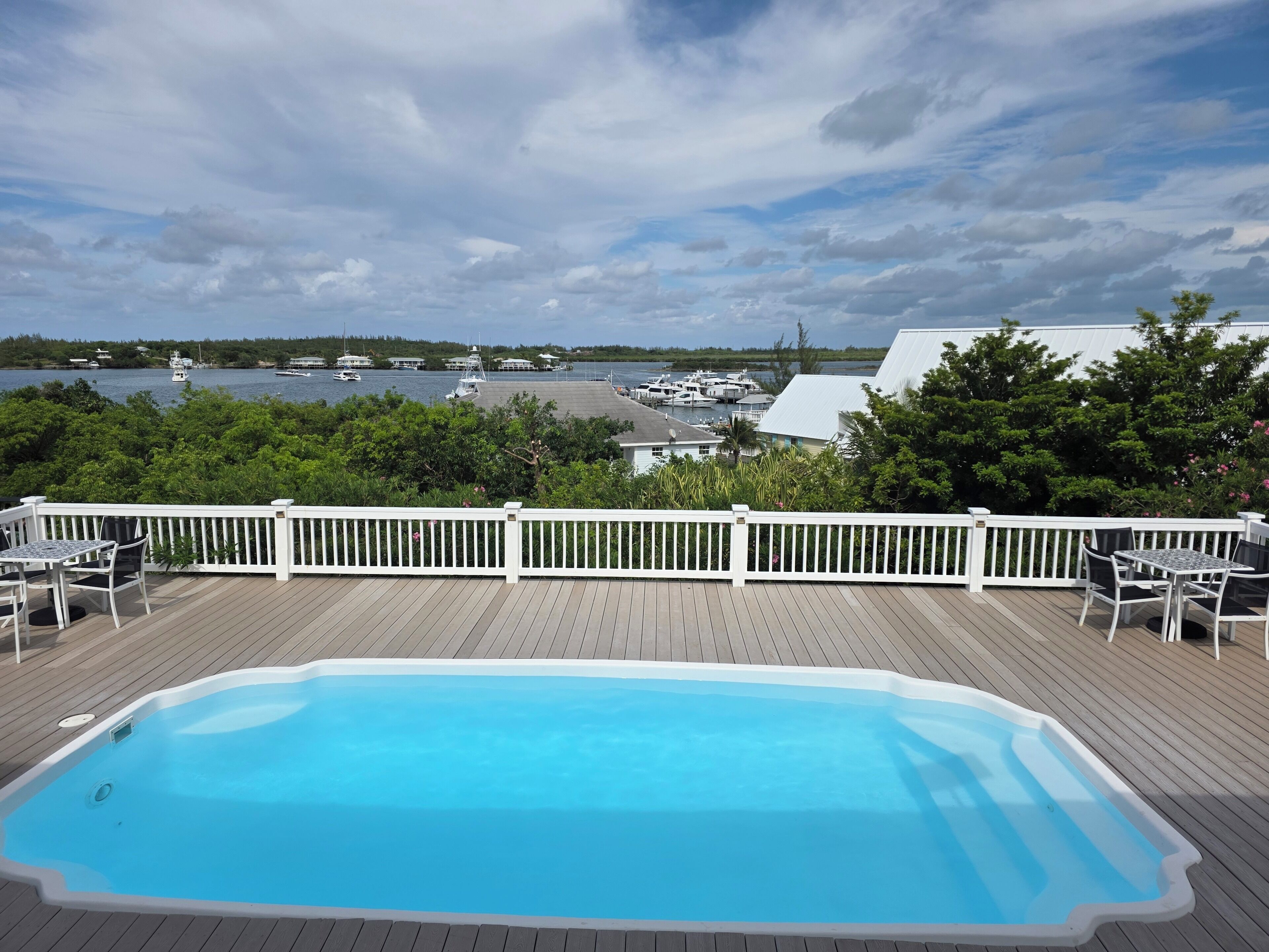 A swimming pool on a wooden deck with a view of boats and water.