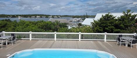 A swimming pool on a wooden deck with a view of boats and water.