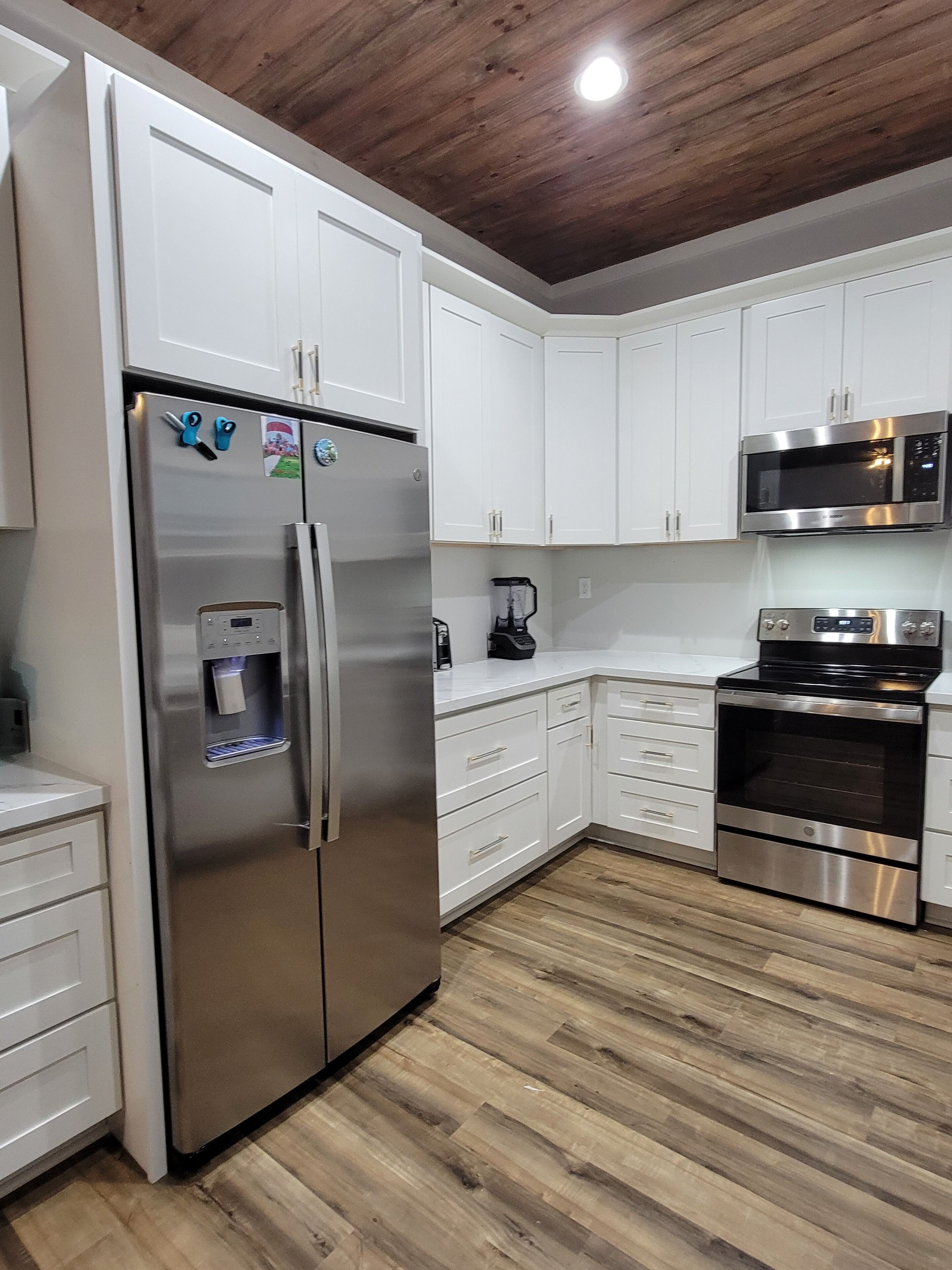 Una cocina moderna con armarios blancos, electrodomésticos de acero inoxidable y techo de madera.