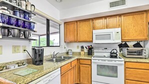 Una cocina con armarios de madera, microondas, estufa, cafetera y tostadora.