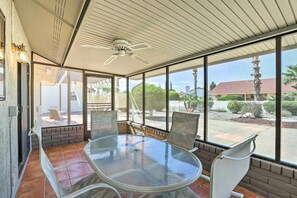 Une terrasse couverte avec une table et des chaises en verre, de grandes fenêtres et un ventilateur de plafond.
