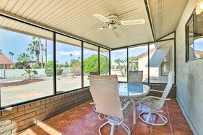 Une terrasse couverte avec une table et des chaises, de grandes fenêtres et un ventilateur de plafond.