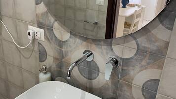 Un bagno con un lavandino bianco, uno specchio e una doccia.