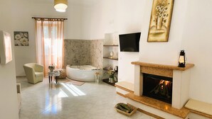Un salón amplio con chimenea, un ventanal con cortinas, un sofá, una mesa de centro y una bañera.