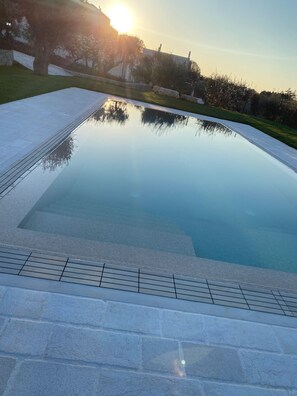 Una piscina cristalina con borde de azulejos, rodeada por un sendero de piedra y una zona de césped.