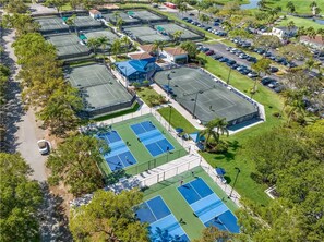 Vista aérea de un complejo deportivo con varias canchas de tenis, zonas de estacionamiento y áreas verdes circundantes.