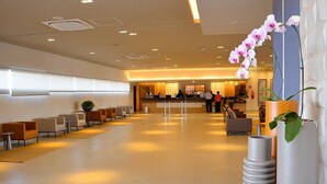 Un amplio vestíbulo con mostrador de recepción, zona de estar y decoración moderna, que incluye un jarrón alto y una exhibición de orquídeas.