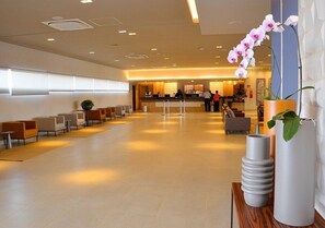 Um lobby amplo com balcão de recepção, área de estar e decoração moderna, incluindo um vaso alto e uma exposição de orquídeas.