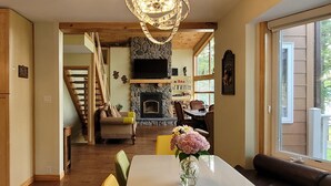 Un salon spacieux avec une cheminée, un escalier en bois et un coin repas agrémenté d’un vase de fleurs.