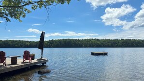 Une jetée en bois s’étendant dans un lac paisible, avec une petite plateforme flottante et des chaises Adirondack rouges sur la jetée.