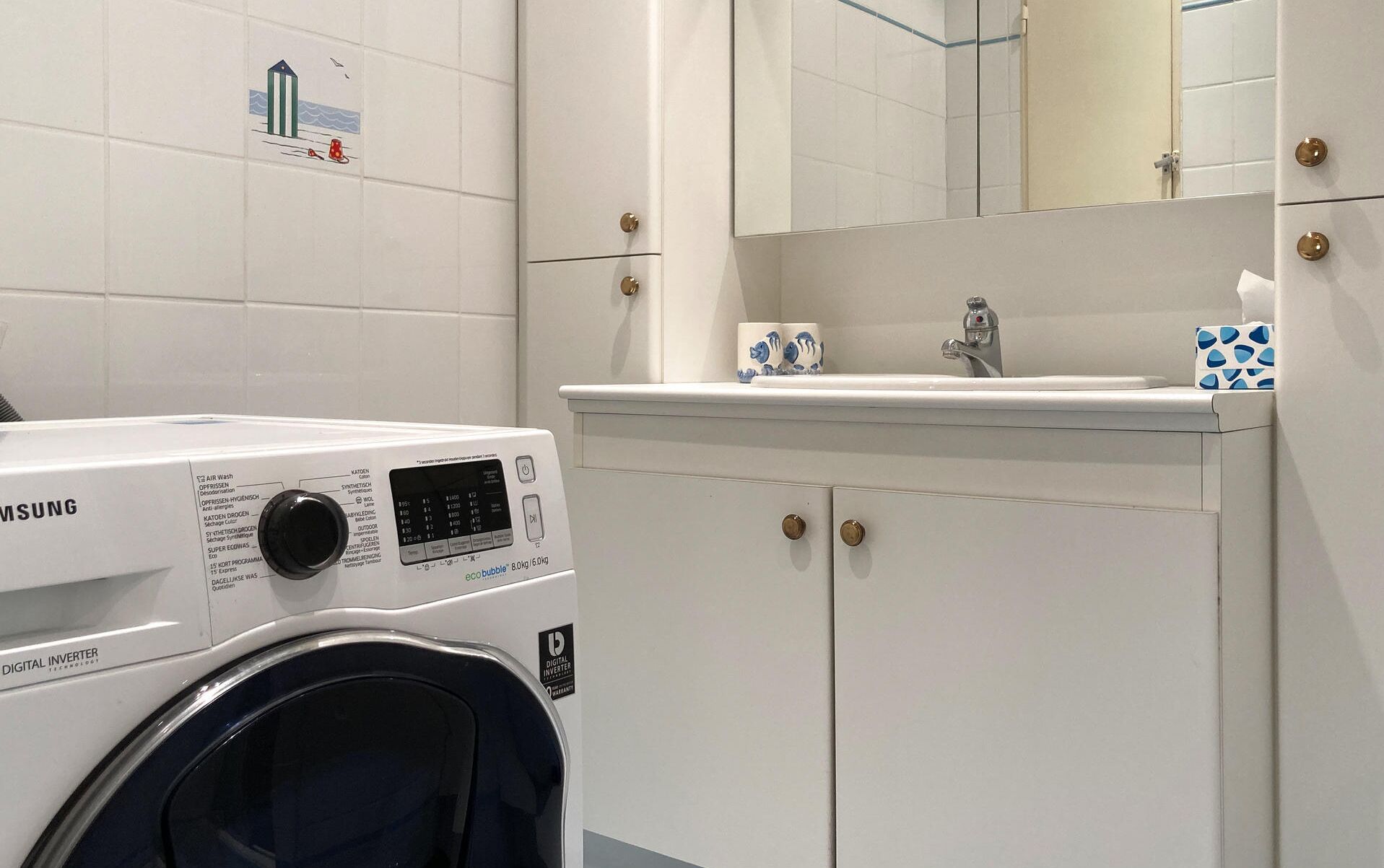 Un bany modern amb una rentadora digital inverter Samsung, un lavabo amb mirall i un armari amb assecador de tovalloles.