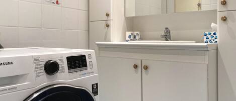 Un bany modern amb una rentadora digital inverter Samsung, un lavabo amb mirall i un armari amb assecador de tovalloles.