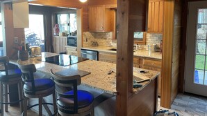 Eine moderne Küche mit Holzschränken, Granit-Arbeitsplatten und einer zentralen Kochinsel mit Barhocker.