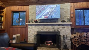 Ein gemütliches Wohnzimmer mit Kamin aus Stein, einem darüber montierten Fernseher und einer bequemen Ledersofa.