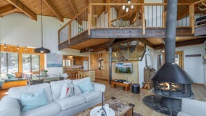 A spacious living area with a high ceiling, a fireplace, a sofa, and a kitchen in the background.