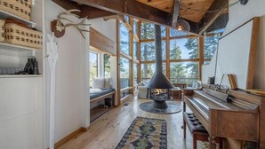 A cozy cabin interior with a fireplace, wooden beams, large windows, and a rustic decor.