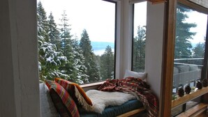 A cozy room with a large window overlooking a snowy forest and a lake.