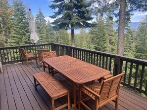 A wooden deck with a table and chairs, surrounded by a black railing, overlooking a forested area. - Tahoe Views & Tahoe Park Access (Tahoe City)