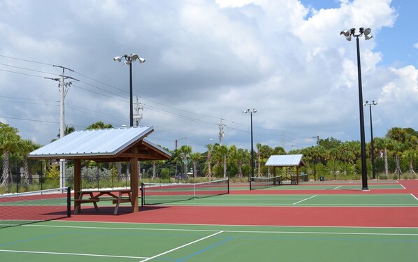 A tennis court with a wooden pavilion, picnic table, and two small shelters.