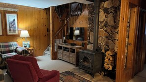 Ein gemütliches Wohnzimmer mit Kamin, Holzwänden, einem Karosobensofa und einem roten Sessel.