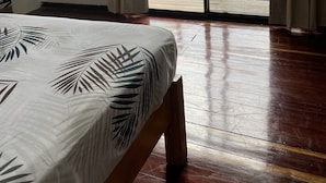 Una habitación con una cama, un televisor montado en la pared y un ventanal corredero que da a un espacio exterior con piscina.