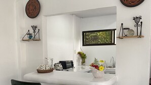 Una cocina con encimera blanca, dos sillas de madera, un fregadero y platos decorativos en la pared.